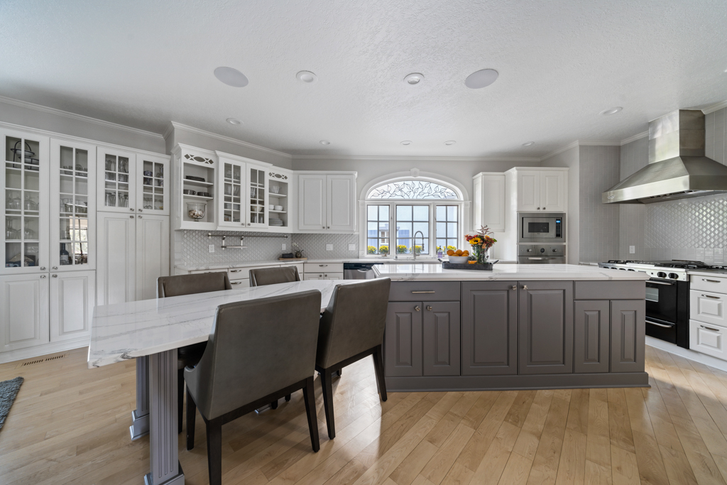 Des Moines kitchen remodel with white cabinetry and white quartz countertops. In the middle of the kitchen stands a gray island and to the left a quartz table.